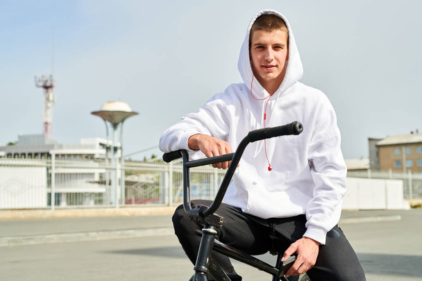 Portrait of handsome young man sitting on bmx bike and looking at camera while posing in sunlight, copy space - Foto, Imagen