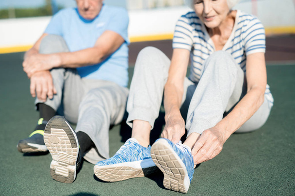 Retrato de seção intermediária de casal de cabelos brancos seniores amarrando sapatos esportivos sentados na pista de corrida ao ar livre, espaço de cópia
 - Foto, Imagem