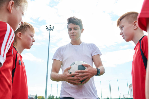 Μέση επάνω πορτρέτο του νεαρού προπονητή που μιλά με την ομάδα ποδοσφαίρου εφήβων δίνοντας οδηγίες πριν από το ματς - Φωτογραφία, εικόνα