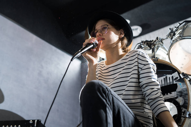 Χαμηλή γωνία πορτρέτο της όμορφης νεαρής γυναίκας που τραγουδά στο μικρόφωνο κατά τη διάρκεια της πρόβα μπάντα στο στούντιο, αντίγραφο χώρου - Φωτογραφία, εικόνα