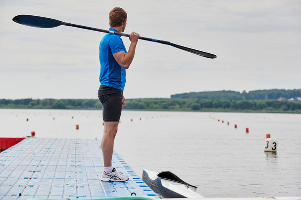 Young athlete in sportswear standing with paddle on the pier and looking at view of calm lake - Photo, Image