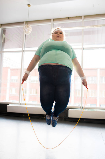 Retrato de comprimento total da jovem mulher obesa pulando corda durante o treino no estúdio de fitness
 - Foto, Imagem