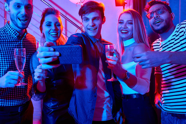 Grupo de mujeres y hombres con estilo moderno que se divierten en la fiesta de vacaciones y tomar selfie con el teléfono
 - Foto, Imagen