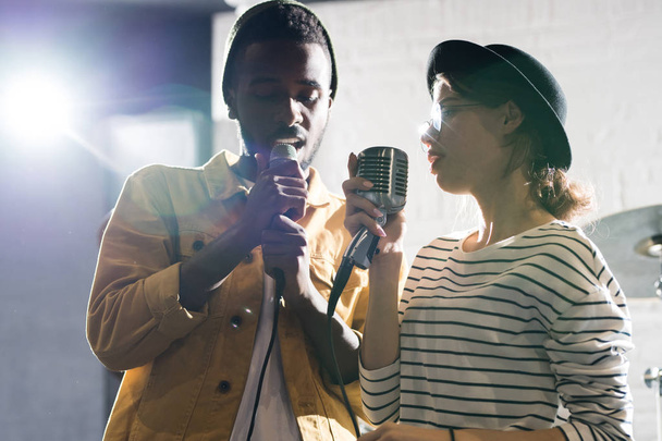 Μέση επάνω πορτρέτο του σύγχρονου νεαρού ζευγαριού που τραγουδούν στη σκηνή απολαμβάνοντας την απόδοση μαζί - Φωτογραφία, εικόνα