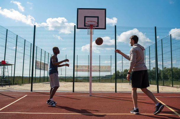 Full length back view portrait of two young men playing basketball in outdoor court , copy space - Fotografie, Obrázek