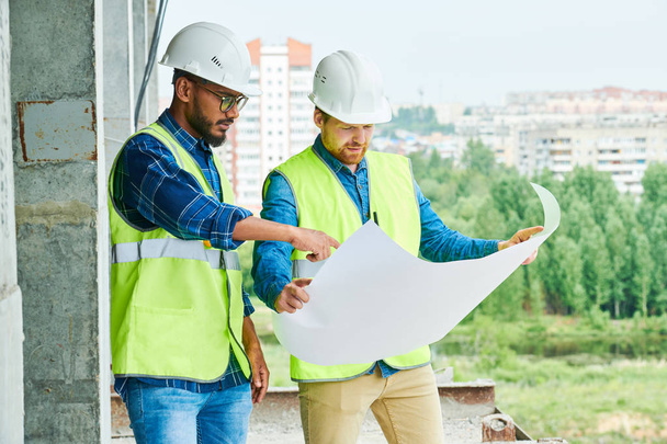 Retrato de dois trabalhadores da construção usando chapéus duros discutindo projeto segurando planos de engenharia no local, espaço de cópia
 - Foto, Imagem