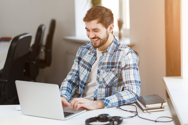 Happy man using laptop at table in office  - Photo, Image