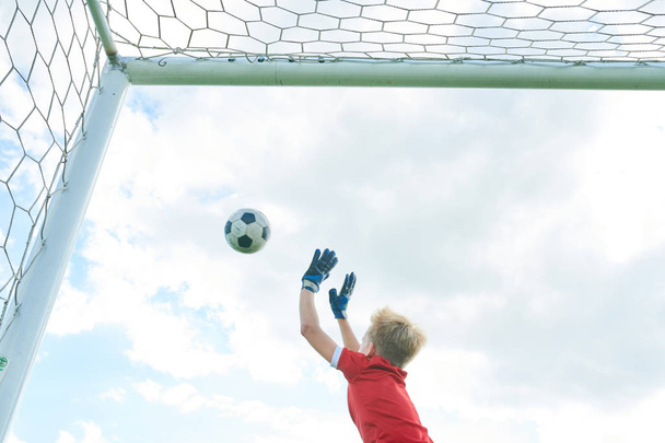 バックビュー十代の少年がジャンプし、ボールをキャッチしながらサッカーの試合でゲートを擁護しながら、スペースをコピー - 写真・画像
