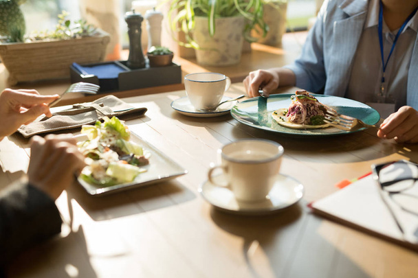 Nahaufnahme von nicht wiederzuerkennenden Geschäftsfrauen, die am Tisch sitzen und köstliche Salate essen, während sie im Restaurant zu Mittag essen - Foto, Bild