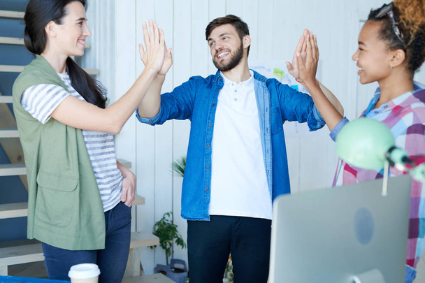 Portrait of three contemporary young people celebrating success and smiling cheerfully doing high five in modern office - Fotografie, Obrázek