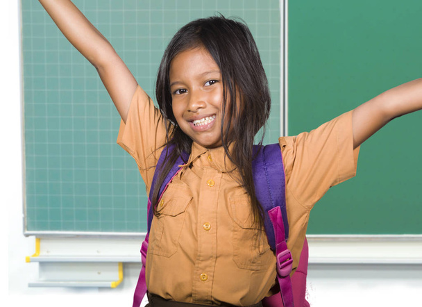 schöne glückliche und aufgeregte weibliche Kind in Schuluniform mit Schülertasche lächelnd fröhlich stehend an der Schultafel in zurück zur Schule und Kindererziehung - Foto, Bild