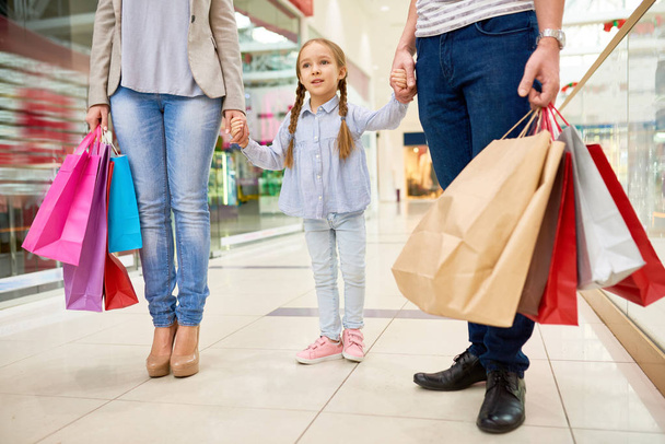 Portrait of happy family shopping in mall, focus on cute little girl holding hands with parents - Foto, Bild