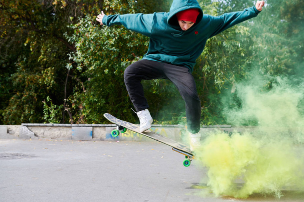 Full length Portret van de moderne tiener doet skateboard stunts in groene rook, kopieerruimte - Foto, afbeelding