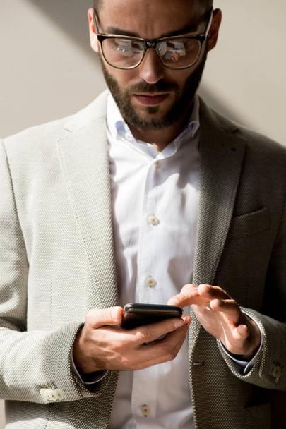 Jovem gerente barbudo em óculos digitando uma mensagem em seu smartphone
 - Foto, Imagem