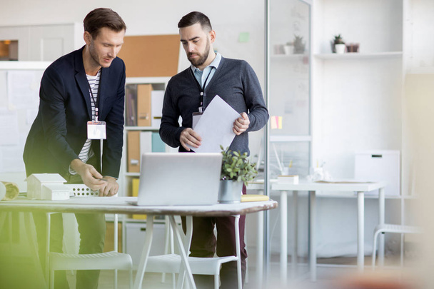 Retrato de dois empresários modernos discutindo o trabalho em pé por mesa no escritório, espaço de cópia
 - Foto, Imagem
