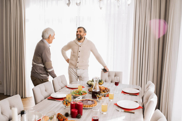 Портрет усміхненого зрілого чоловіка, який розмовляє з батьком стоїть за великим обіднім столом під час сімейного святкування, копіювання простору
 - Фото, зображення