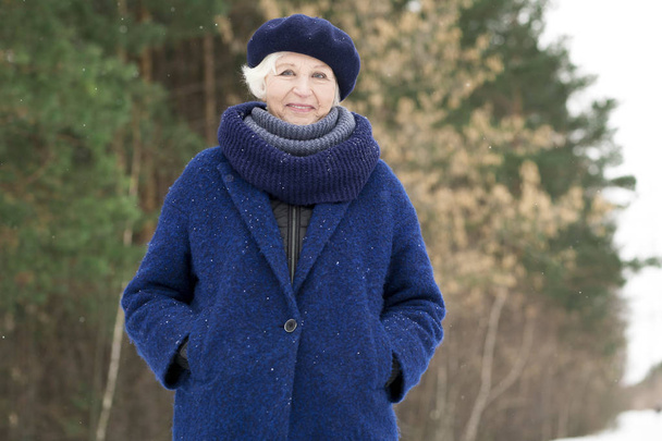 Talia się portret nowoczesnej starszy kobieta stwarzające w zimie lasu i uśmiechając się w aparacie, przestrzeń kopiowania - Zdjęcie, obraz