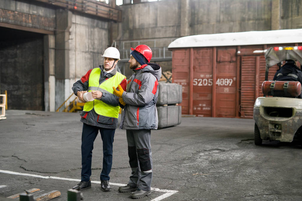 Retrato de comprimento total de dois trabalhadores industriais vestindo jaquetas quentes e hardhats discutindo a produção em pé na oficina, espaço de cópia
 - Foto, Imagem