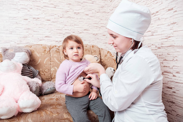 Femme médecin écoute l'enfant avec stéthoscope à la maison
.  - Photo, image