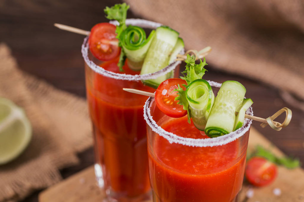 Two glasses of tomato juice decorated with fresh tomatoes, cucumber and leaves on a wooden background - Fotó, kép