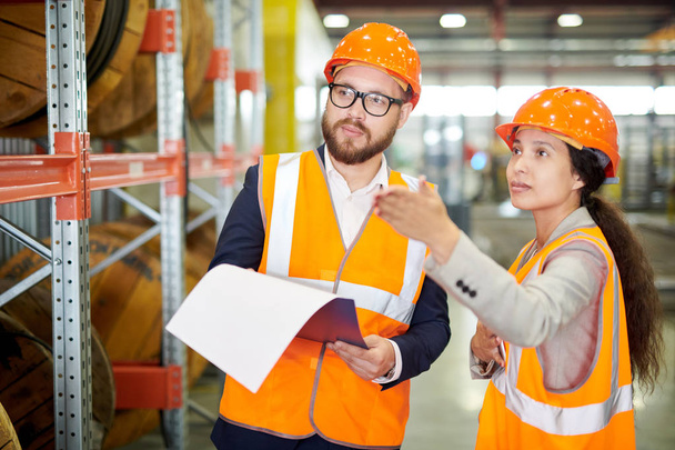 Waist up portrait of female factory worker talking to bearded businessman wearing hardhat and pointing away, copy space - Foto, immagini