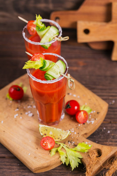 Two glasses of tomato juice decorated with fresh tomatoes, cucumber and leaves on a wooden background - Φωτογραφία, εικόνα
