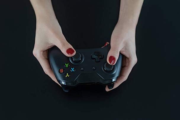 Pohled z rukou žena s červenými nehty na prstech drží loga zdarma moderní herní ovladač pro přehrávání digitálních video her izolované na černou pro zábavu shora volný čas zábava  - Fotografie, Obrázek
