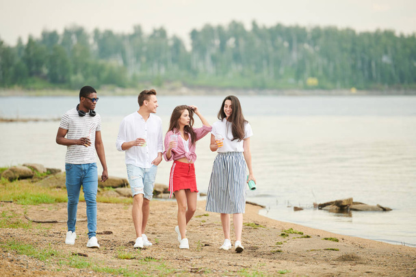 Monietniset nuoret nauttivat vapaa-ajastaan luonnossa. He kävelevät rannalla.
 - Valokuva, kuva