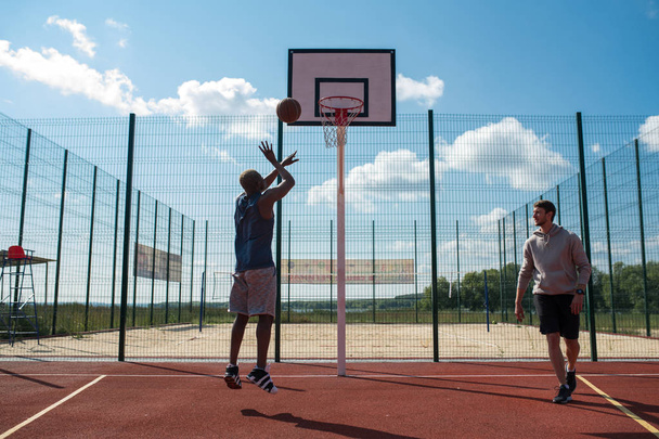 Retrato completo de dos hombres jóvenes jugando baloncesto en la cancha al aire libre, se centran en el hombre africano disparando slam dunk en primer plano, espacio de copia
 - Foto, imagen