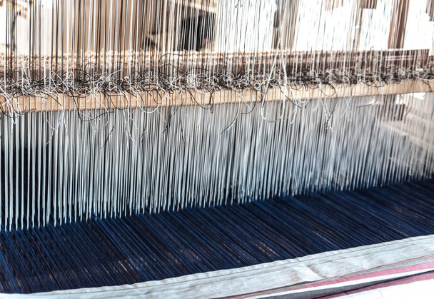 Detalle de un antiguo telar de tejido vintage tradicional con muchas cuerdas de algodón atadas a un marco de madera como herramienta de fabricación artesanal profesional para la producción de tejidos hechos a mano en un taller textil
 - Foto, Imagen
