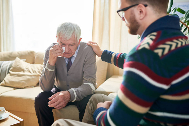 Psicólogo empático consolando a un hombre mayor y acariciando su hombro mientras lo apoya y anima durante la sesión de terapia
 - Foto, imagen