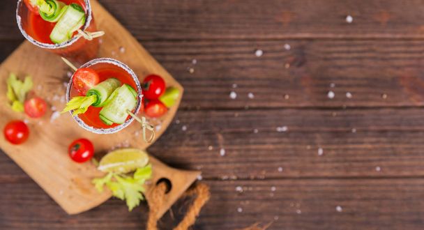 Two glasses of tomato juice decorated with fresh tomatoes, cucumber and leaves on a wooden background - Fotoğraf, Görsel