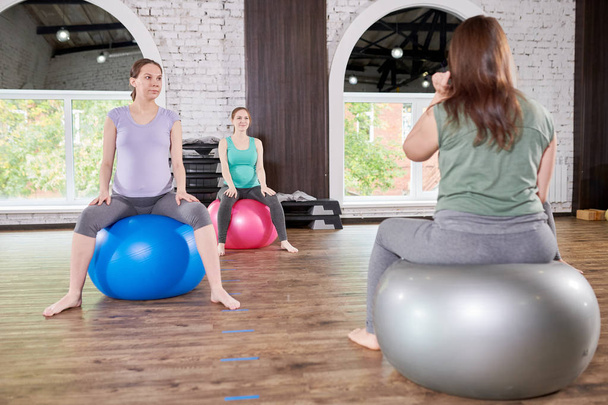 Full length portrait of group of pregnant young women sitting on fitness balls and listening to prenatal yoga instructor, copy space - Photo, Image