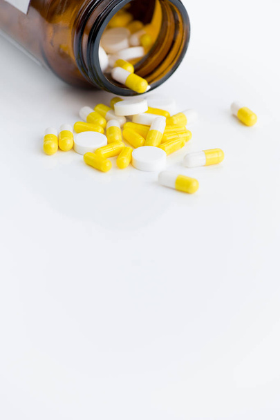 Close-up de cápsulas de medicação sortidas derramando do frasco sobre fundo branco, espaço de cópia
 - Foto, Imagem