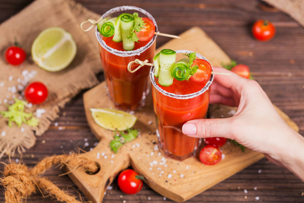 Two glasses of tomato juice decorated with fresh tomatoes, cucumber and leaves on a wooden background - Valokuva, kuva