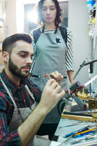 Portret van jonge man shaping Glass terwijl het maken van kralen voorhand gemaakte sieraden in opzet Studio - Foto, afbeelding