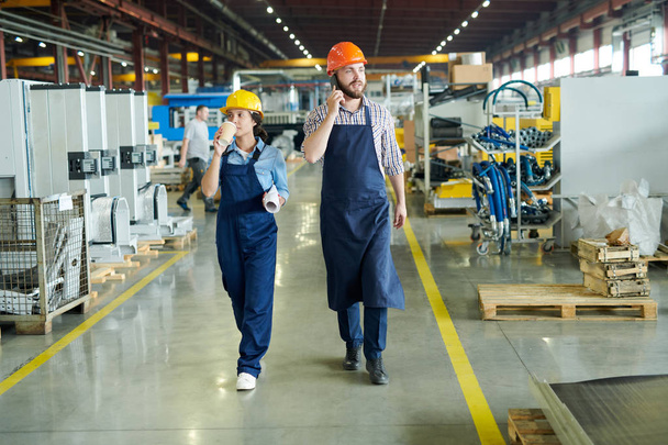 Retrato de longitud completa de dos trabajadores de la fábrica caminando hacia la cámara a través del taller de fábrica moderna
 - Foto, imagen