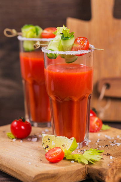 Two glasses of tomato juice decorated with fresh tomatoes, cucumber and leaves on a wooden background - Foto, Imagem