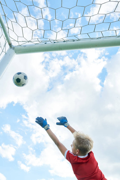バックビュー十代の少年跳躍とサッカーの試合でゲートを擁護しながらボールをキャッチ - 写真・画像