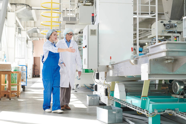 Retrato de larga duración de una joven trabajadora mostrando unidades de máquinas en fábrica a una mujer mayor, espacio de copia
 - Foto, Imagen