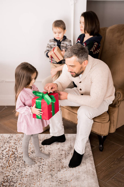 Портрет щасливого зрілого батька, що дарує подарунок маленькій дівчинці, сцена сімейного обміну подарунками напередодні Різдва
 - Фото, зображення
