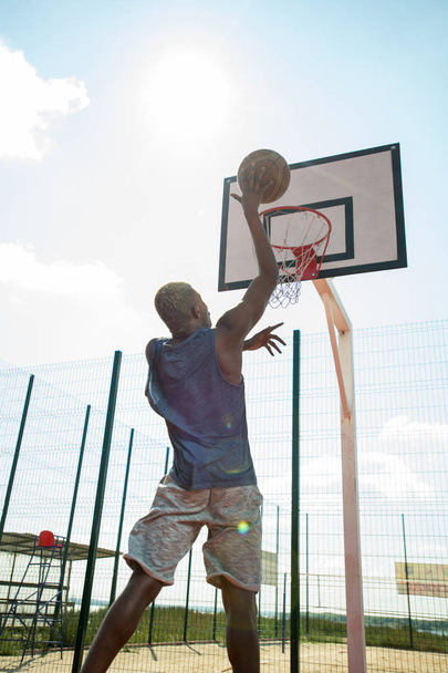 Motivational back view portrait of African young man shooting slam dunk in basketball court outdoors - Photo, Image