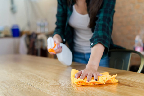 Nahaufnahme einer Frau, die ein Haus putzt. Während sie auf dem Tisch putzt, wischt sie Staub mit einem Spray und einem orangefarbenen Stoff ab. Hausreinigungskonzept. - Foto, Bild