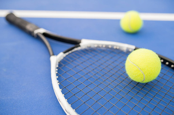 Sports background of yellow tennis ball  and racket laying on blue floor in court, copy space - Photo, Image