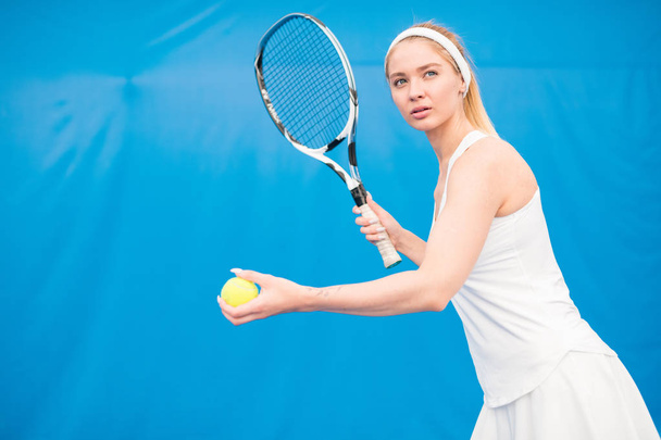Waist up  portrait of female tennis player serving ball and holding racket in indoor court, copy space - Foto, Imagem