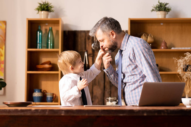 lustiger gutaussehender Vater und lächelnder Sohn beim Rollenspiel in der Küche: verspielter Vater zeigt auf Nase, während sein Sohn den Zeigefinger hält - Foto, Bild