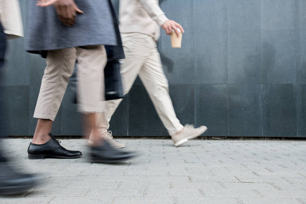 Close-up de pessoas de negócios irreconhecíveis andando pela rua enquanto se apressam para o trabalho de manhã, movimento turvo
 - Foto, Imagem