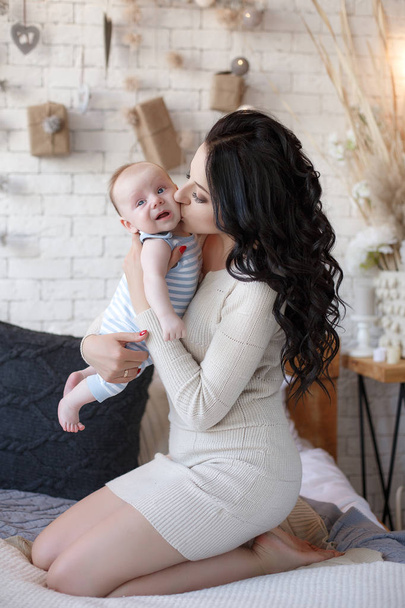 Young mother holding her newborn child. Woman and new born boy relax in a white bedroom. A young mother gently holds her newborn son in her arms. Family at home. Young mother playing whith her newborn son - Foto, immagini