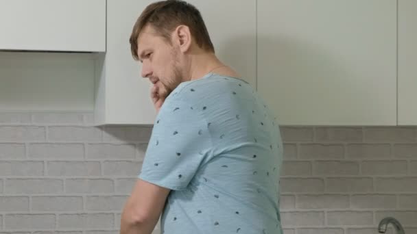 A man in pajamas drinking water in the kitchen. Morning - Materiał filmowy, wideo