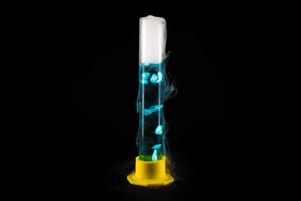 Крупный план стеклянной трубки с голубой жидкостью с холодным паром, выливающимся из нее на черном фоне, концепция химического эксперимента
 - Фото, изображение